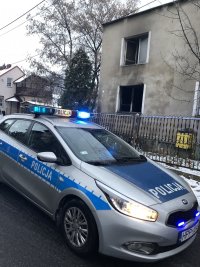 radiowóz policyjny na tle  spalonego domu