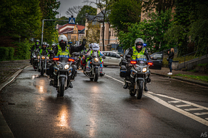 na zdjęciach dwóch umundurowanych policjantów ruchu drogowego jadący na oznakowanych policyjnych motocyklach zabezpieczający paradę motocyklową. Jeden z policjantów na motorze trzyma rękę w górze.